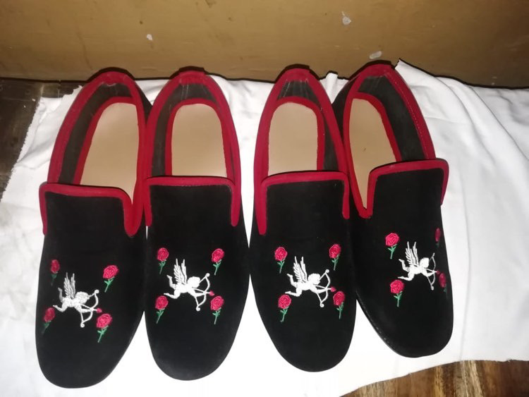 Four black slippers with embroidered white fairy and pink flowers, lined up on a white cloth.