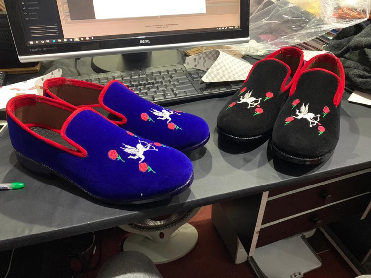 Two pairs of slippers with animal designs on a desk, one blue with a white animal and red accents, one black with a white animal and red accents.