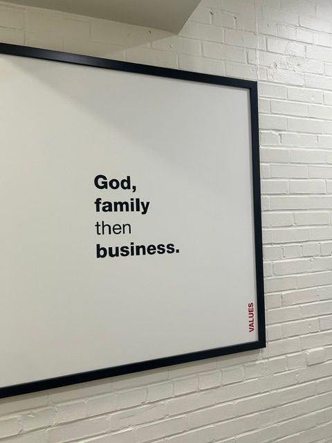 Framed whiteboard with black border, displaying text about family and business, mounted on a white tiled wall.