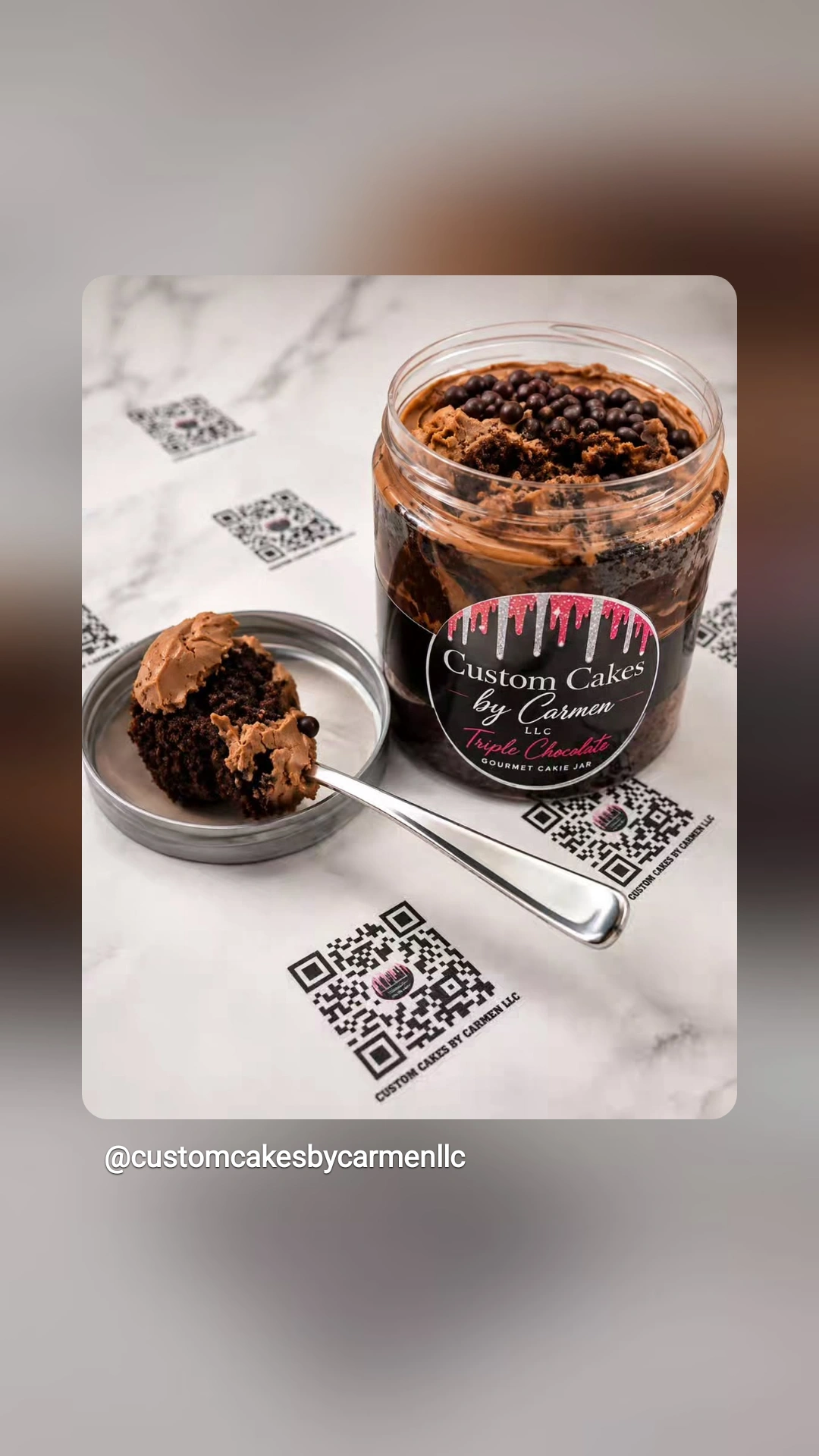 Glass jar of chocolate dessert with a spoon and QR codes on paper, label reads 'Custom Cakes by Carmen'.
