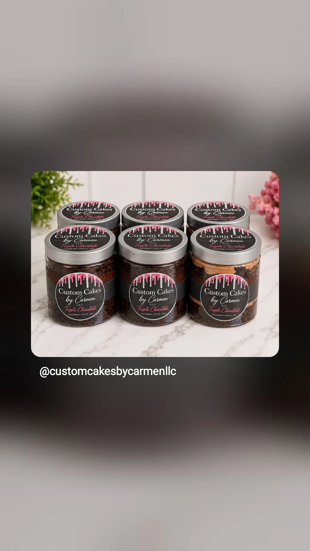 Six jars of caramel with black labels and pink accents, arranged in two rows on a white surface, with pink flowers in the background.