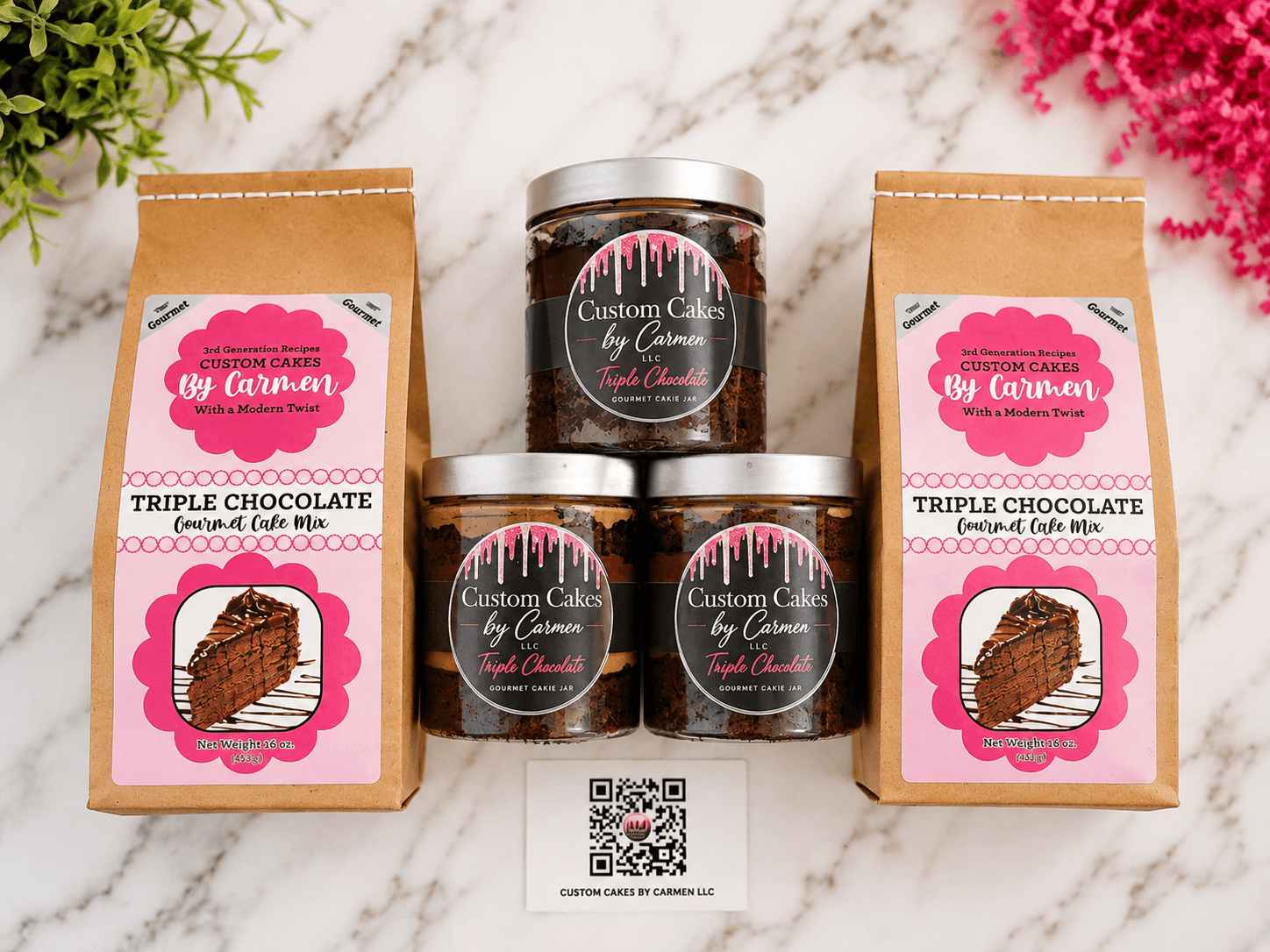 Two packages of triple chocolate cake mix and two jars of custom cake flavoring on a marble surface, with green and pink plants nearby.