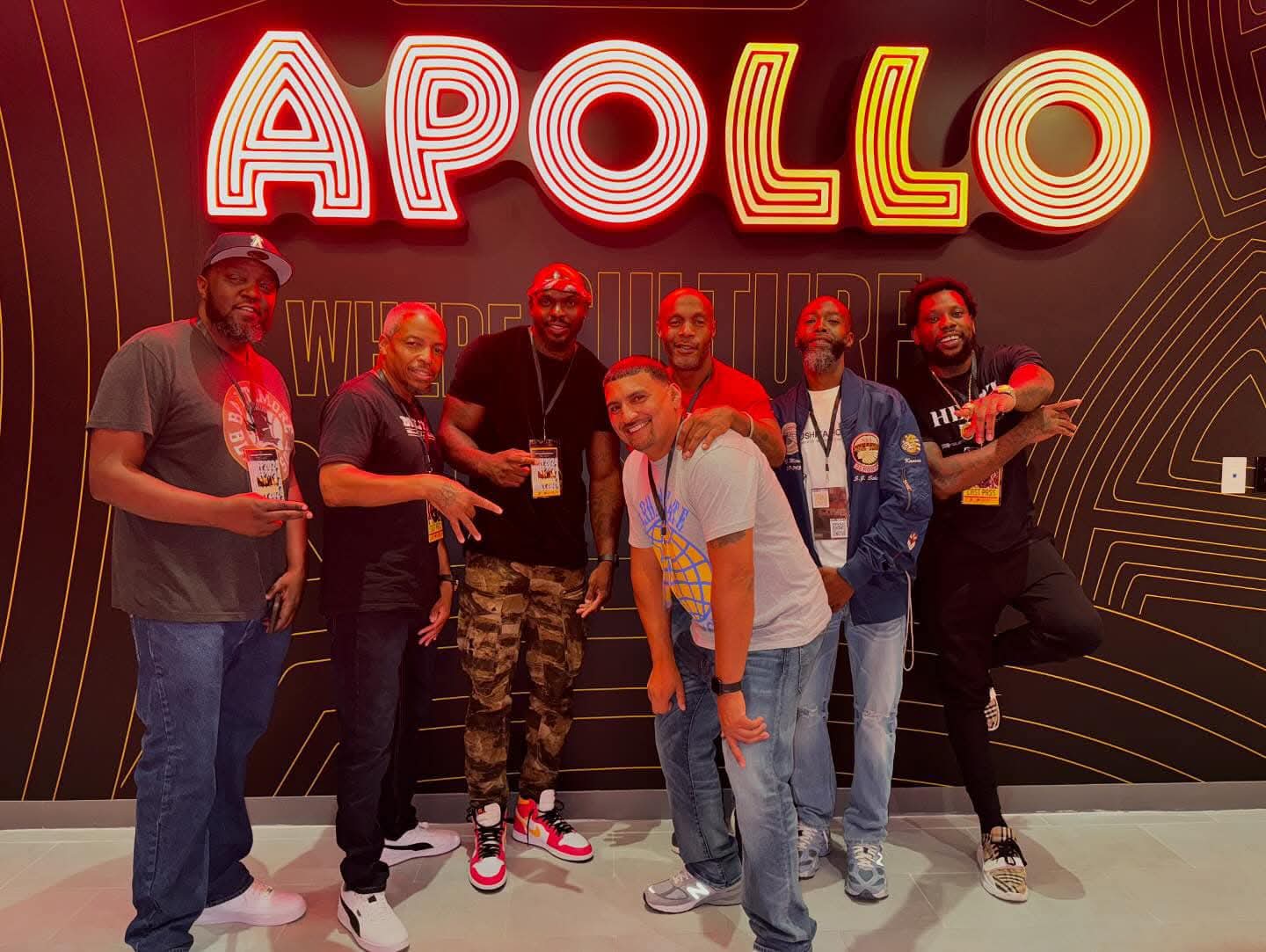 Group of six people standing in front of a sign that says 'APOLLO' with a black background and red and yellow lettering.
