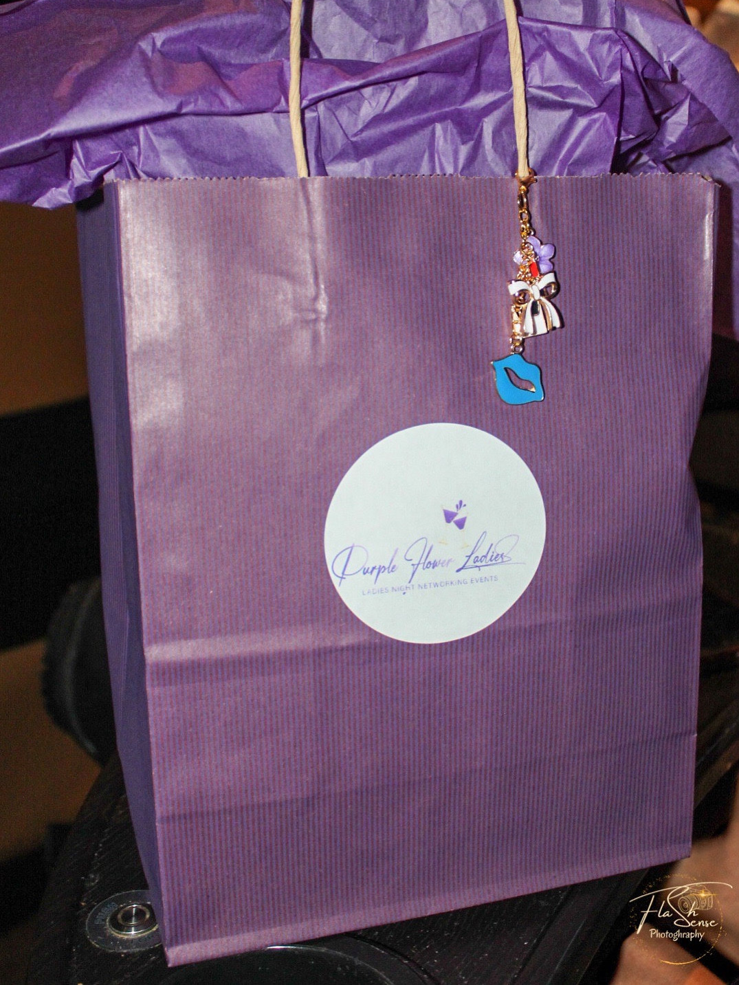 Purple gift bag with a white circular label and a small charm hanging from the handle.