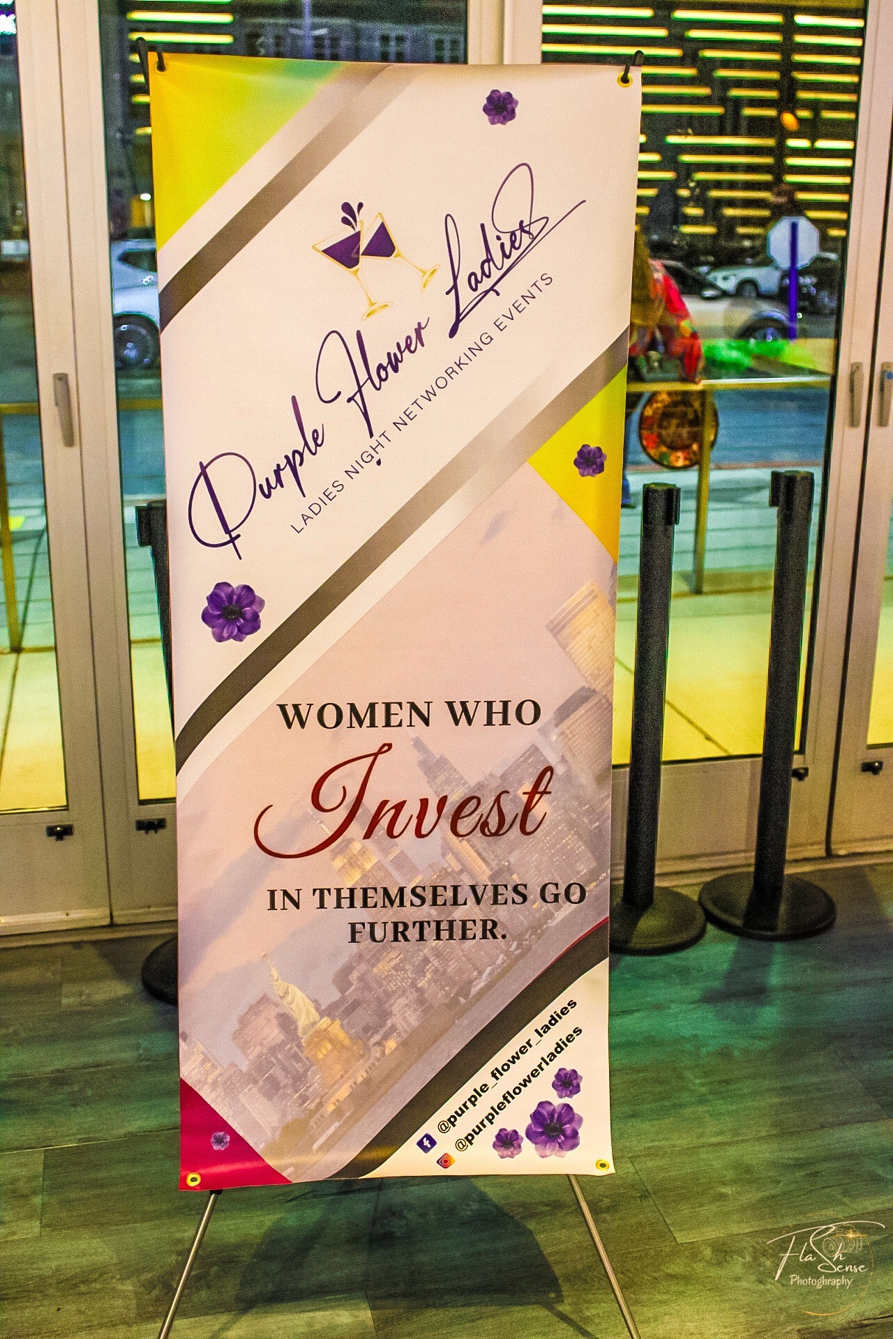 Vertical sign with purple flowers, text about women investing in themselves, and a background with abstract patterns.
