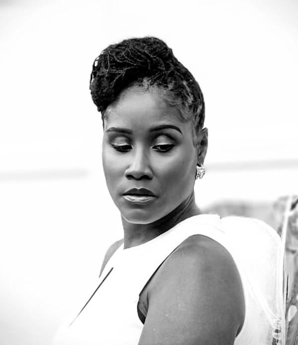 Portrait of a woman with styled hair, wearing a sleeveless top, looking downward, with a neutral expression.