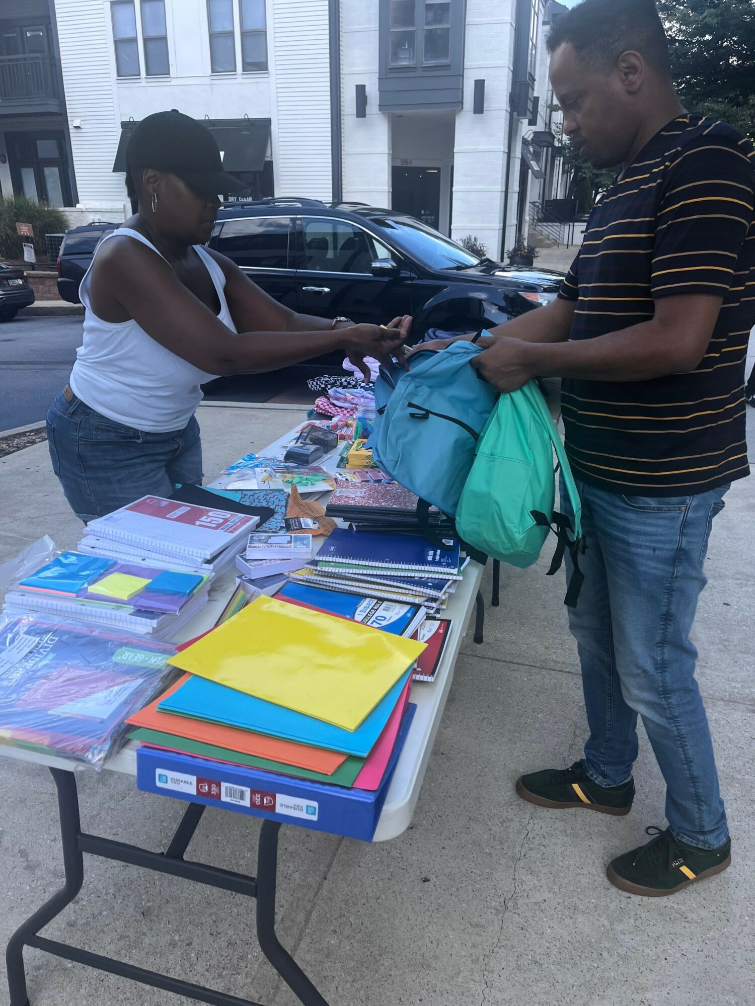 Two people at a table with colorful folders and papers, outdoors in an urban area.