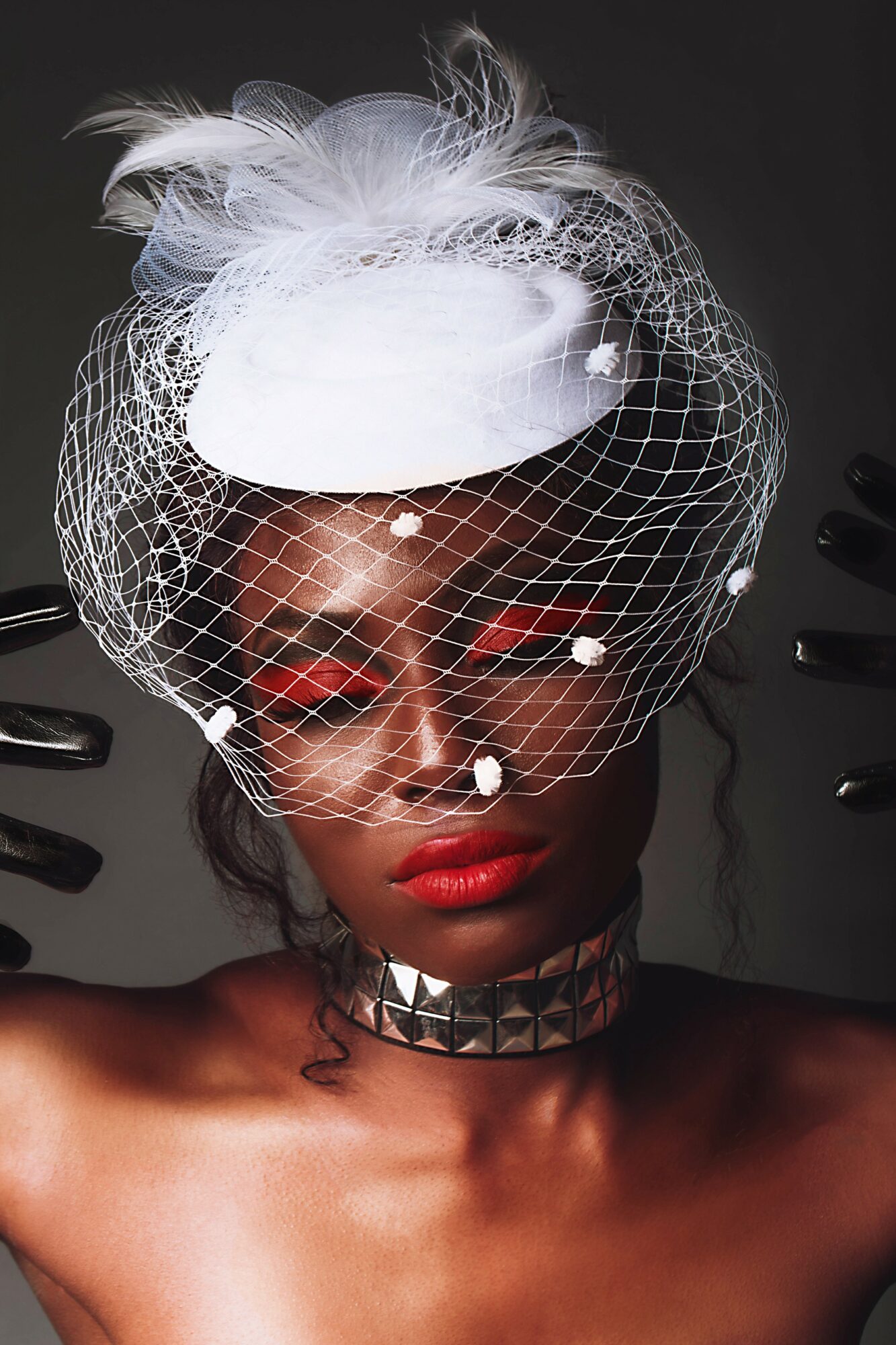 Woman with white hat, netting, and red lipstick, wearing a choker, against a dark background.