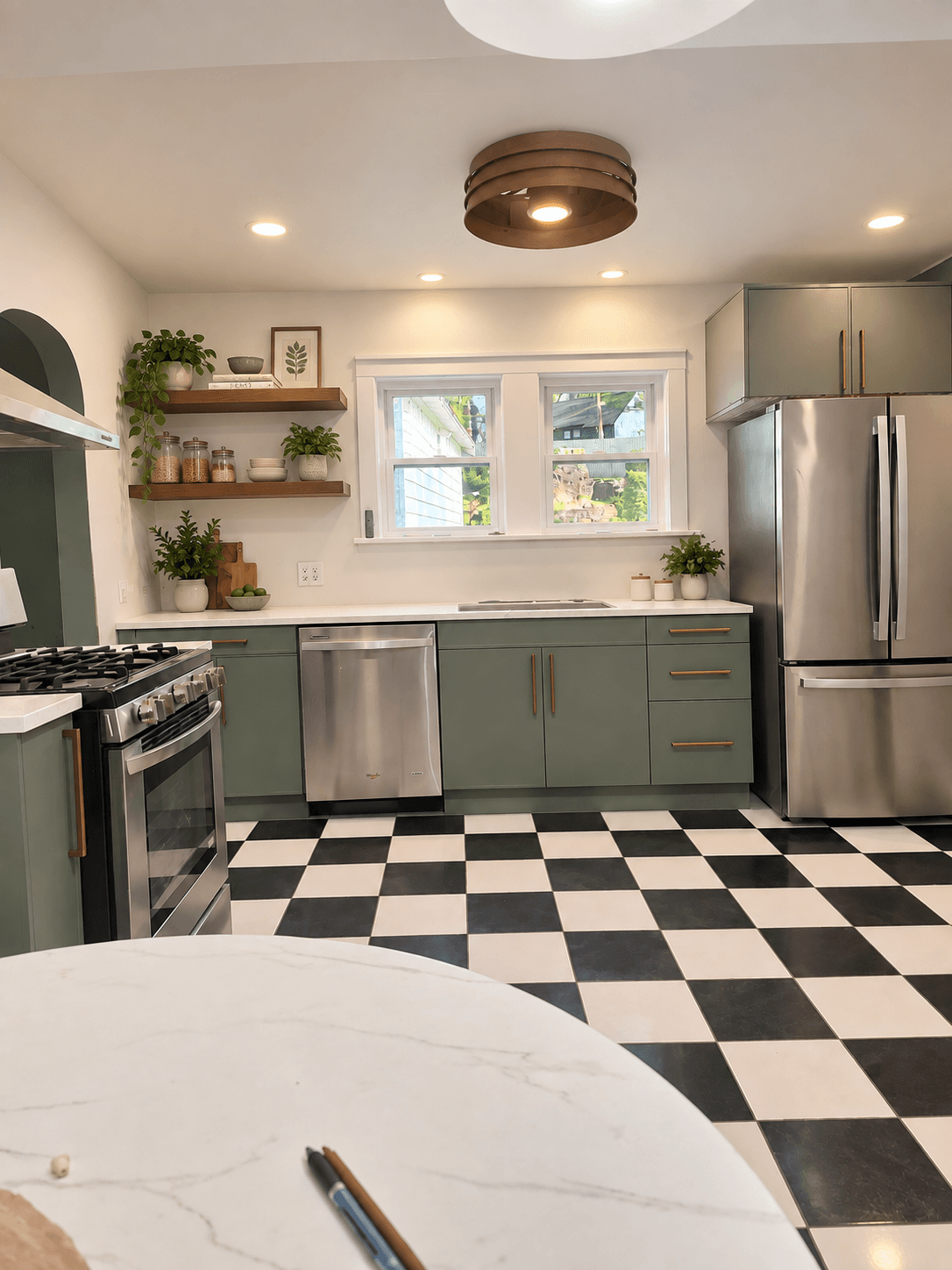 Kitchen with green cabinets, black and white checkered floor, stainless steel appliances, and a window above the sink.