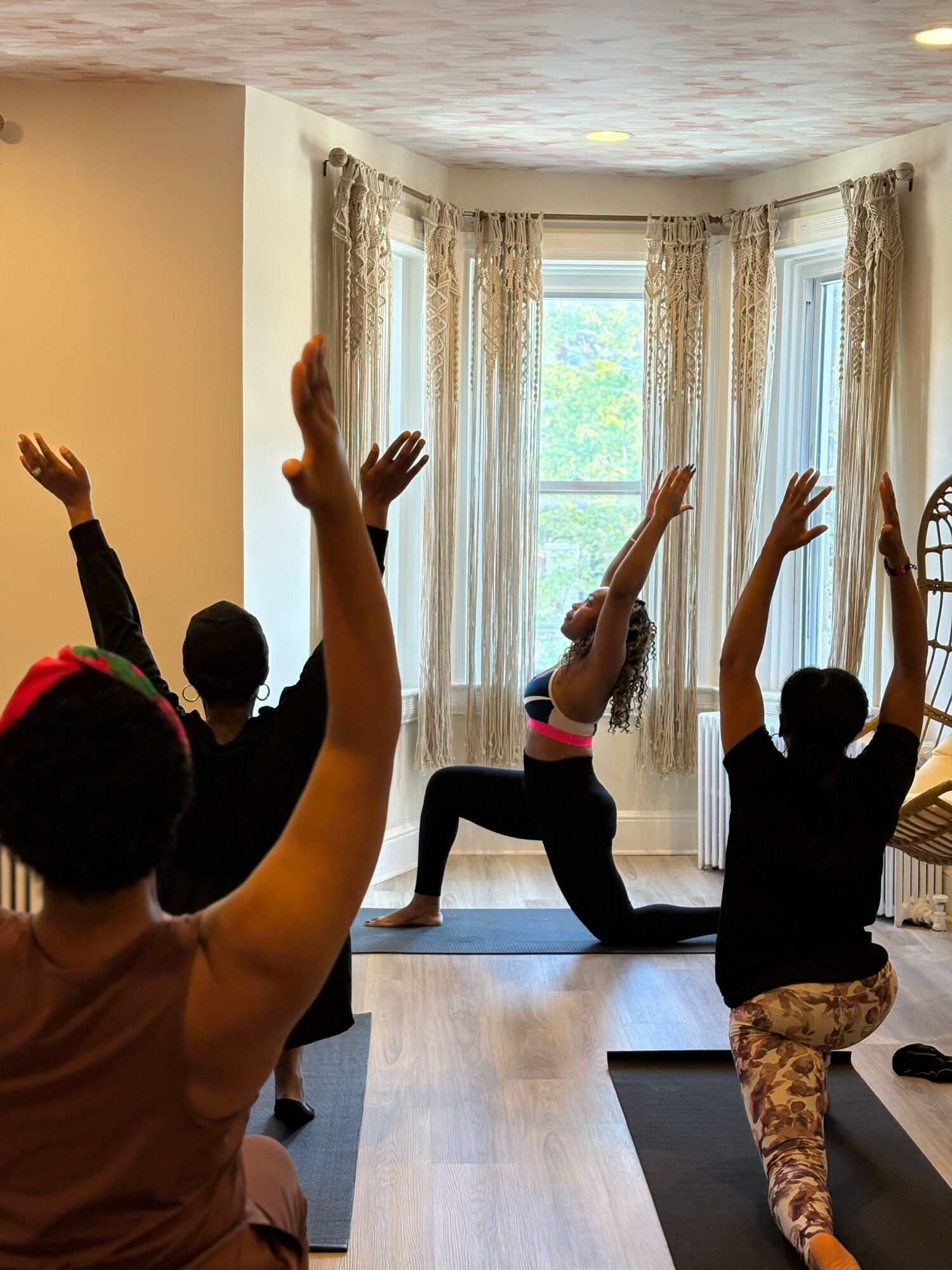 Children participating in a yoga class with raised arms in a bright room with large windows and curtains.