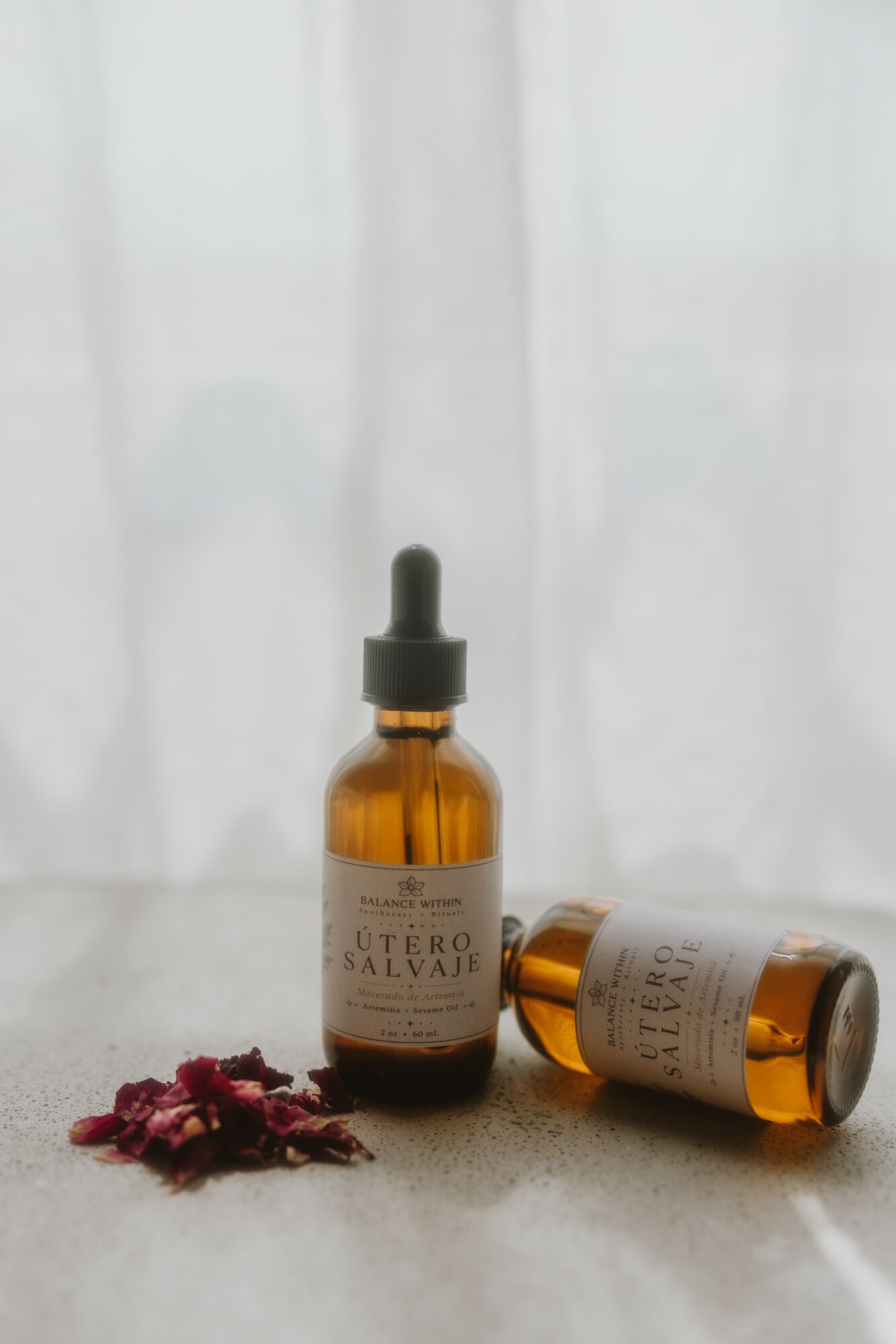 Two amber glass bottles with dropper caps, one standing and one lying down, on a light surface with dried flowers nearby.