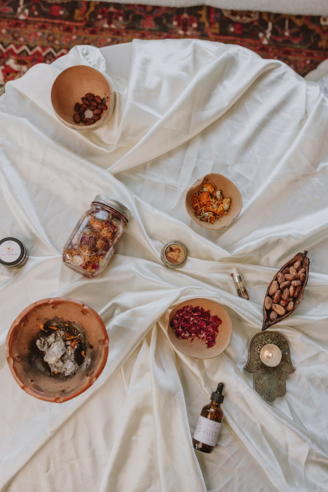 Assorted snacks and desserts on white fabric, including bowls with cereal, berries, and chocolate, along with a jar and a small bottle.