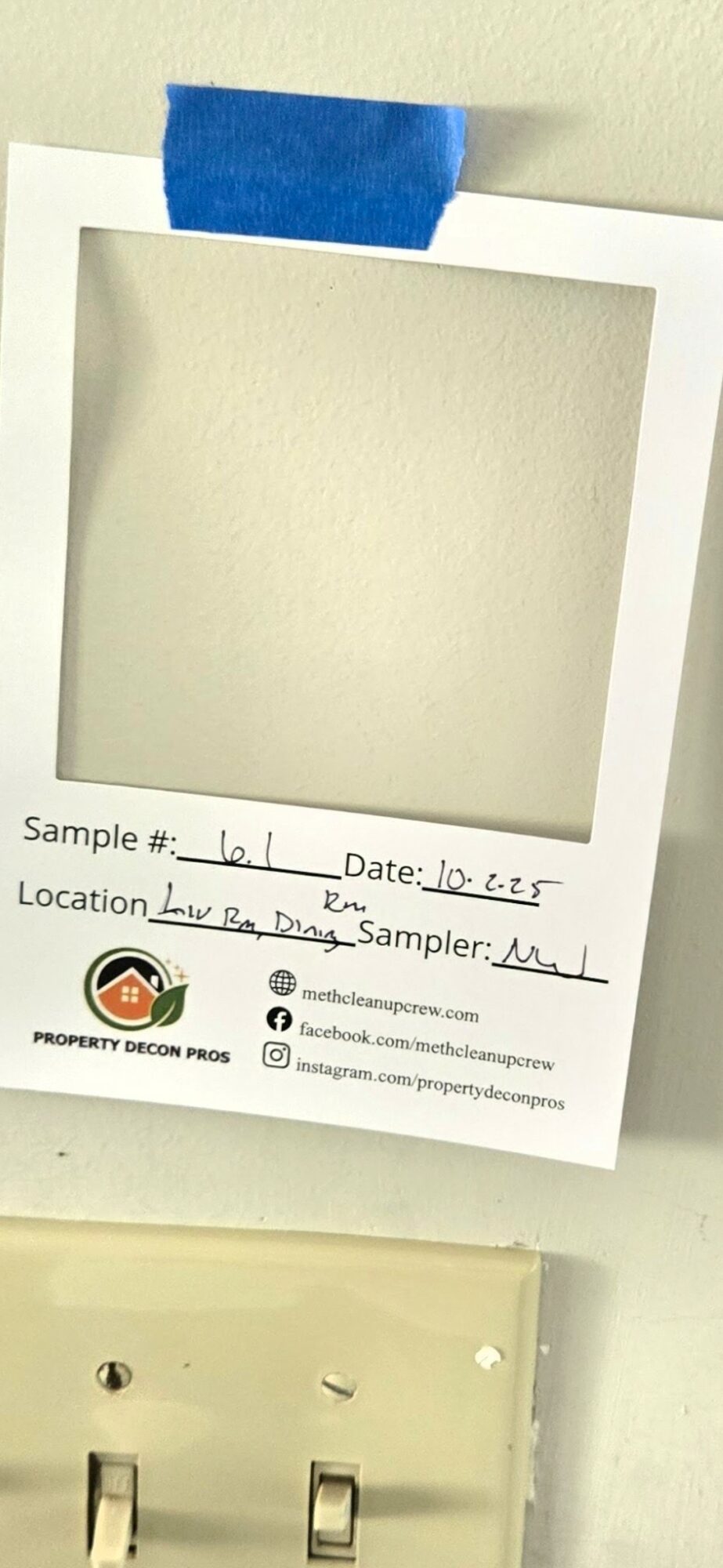 Polaroid-style photo frame taped to a wall with handwritten sample, date, location, and sampler details visible.