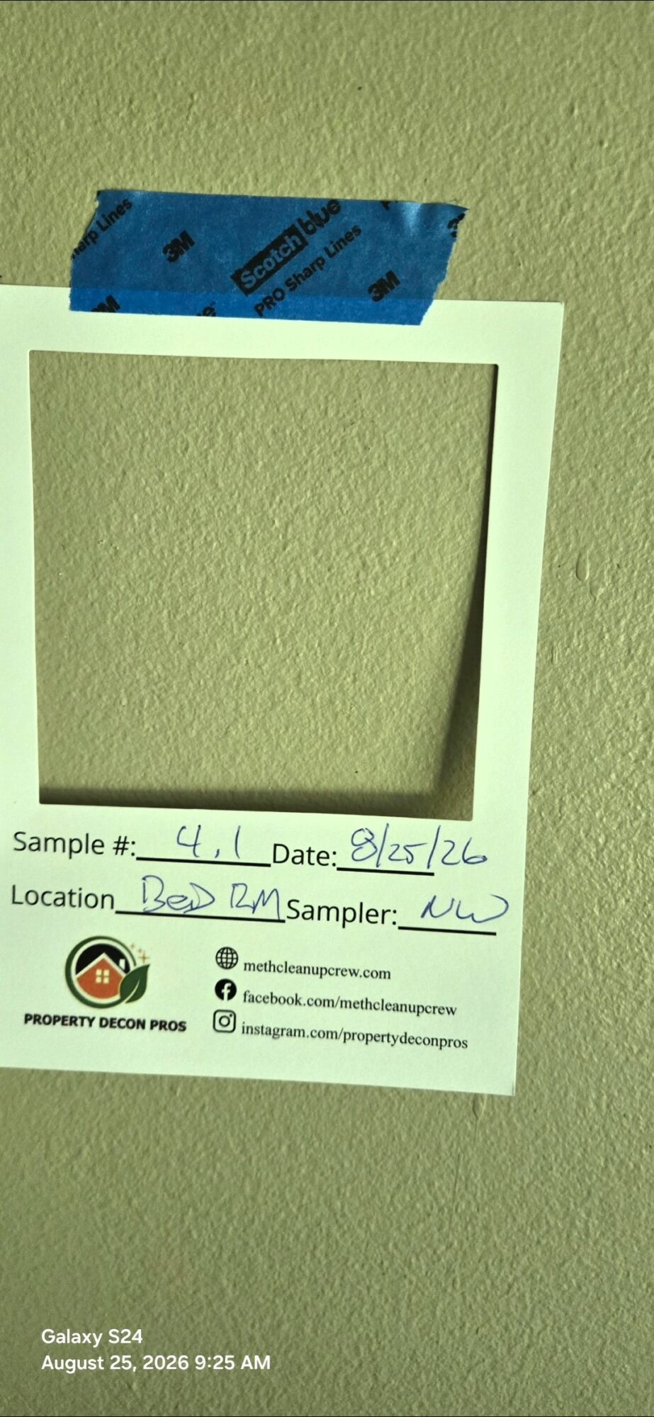 Polaroid-style photo frame taped to a wall with blue tape, containing handwritten sample, date, location, and sampler information.