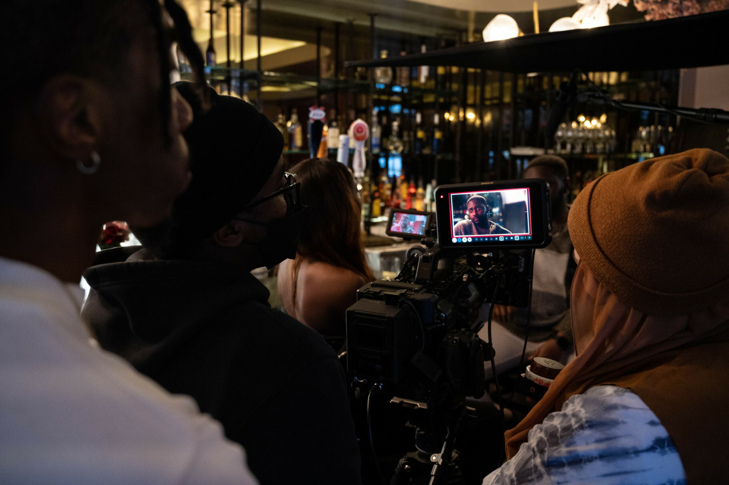 Group of people filming or photographing in a dimly lit indoor setting with equipment and screens visible.