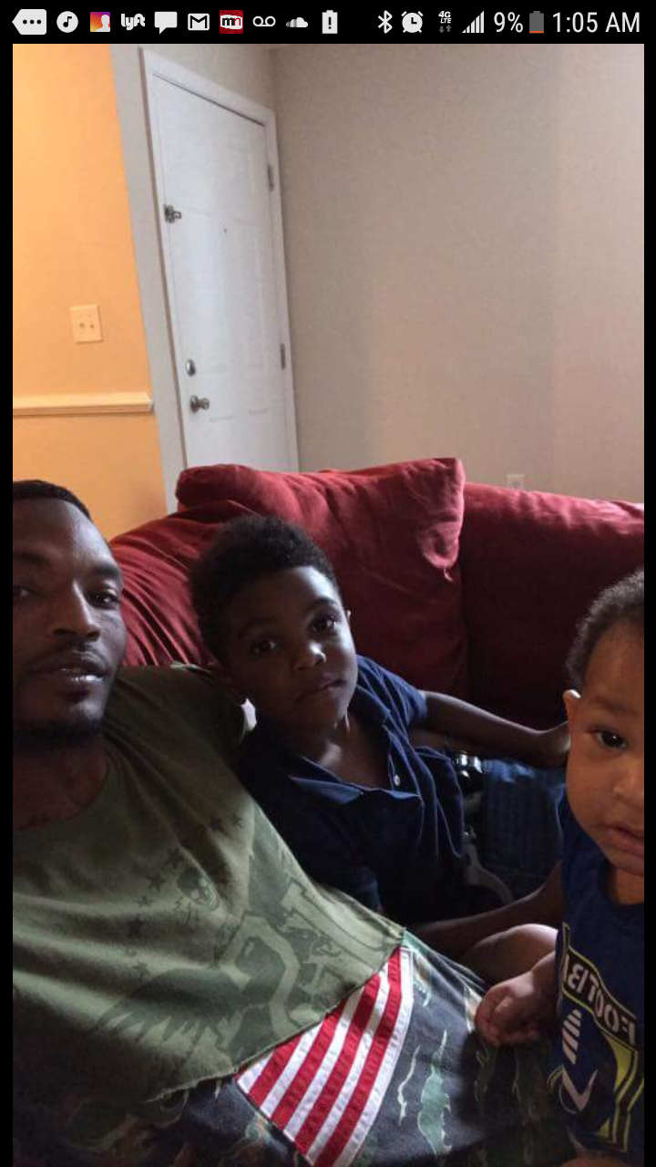 Three people sitting on a red couch in a living room, with a door in the background.