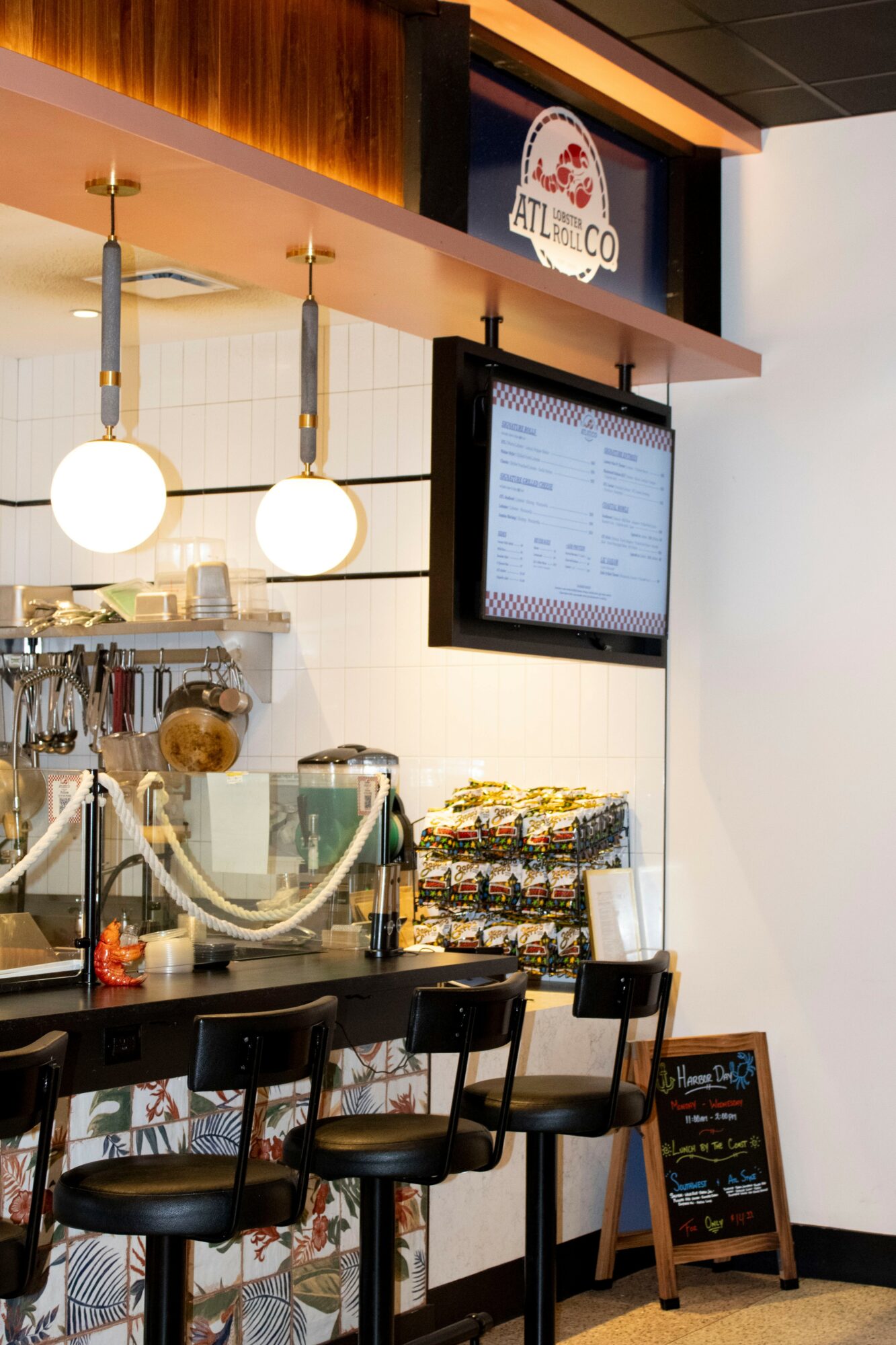 Counter with three black stools, menu screen, and hanging lights inside a cafe or restaurant.