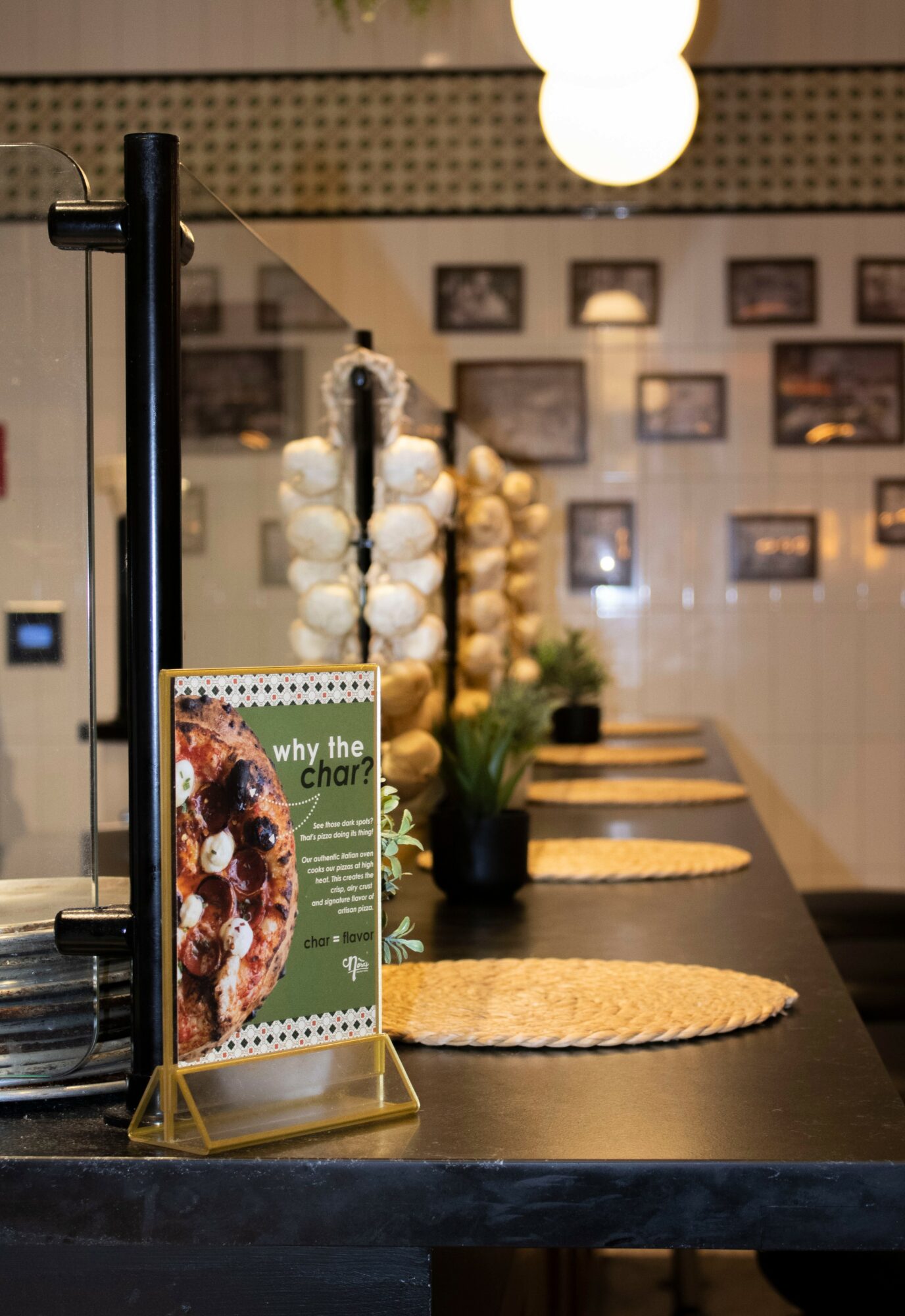 Counter with a menu stand, potted orchid, and woven placemats, with framed pictures on the wall in the background.