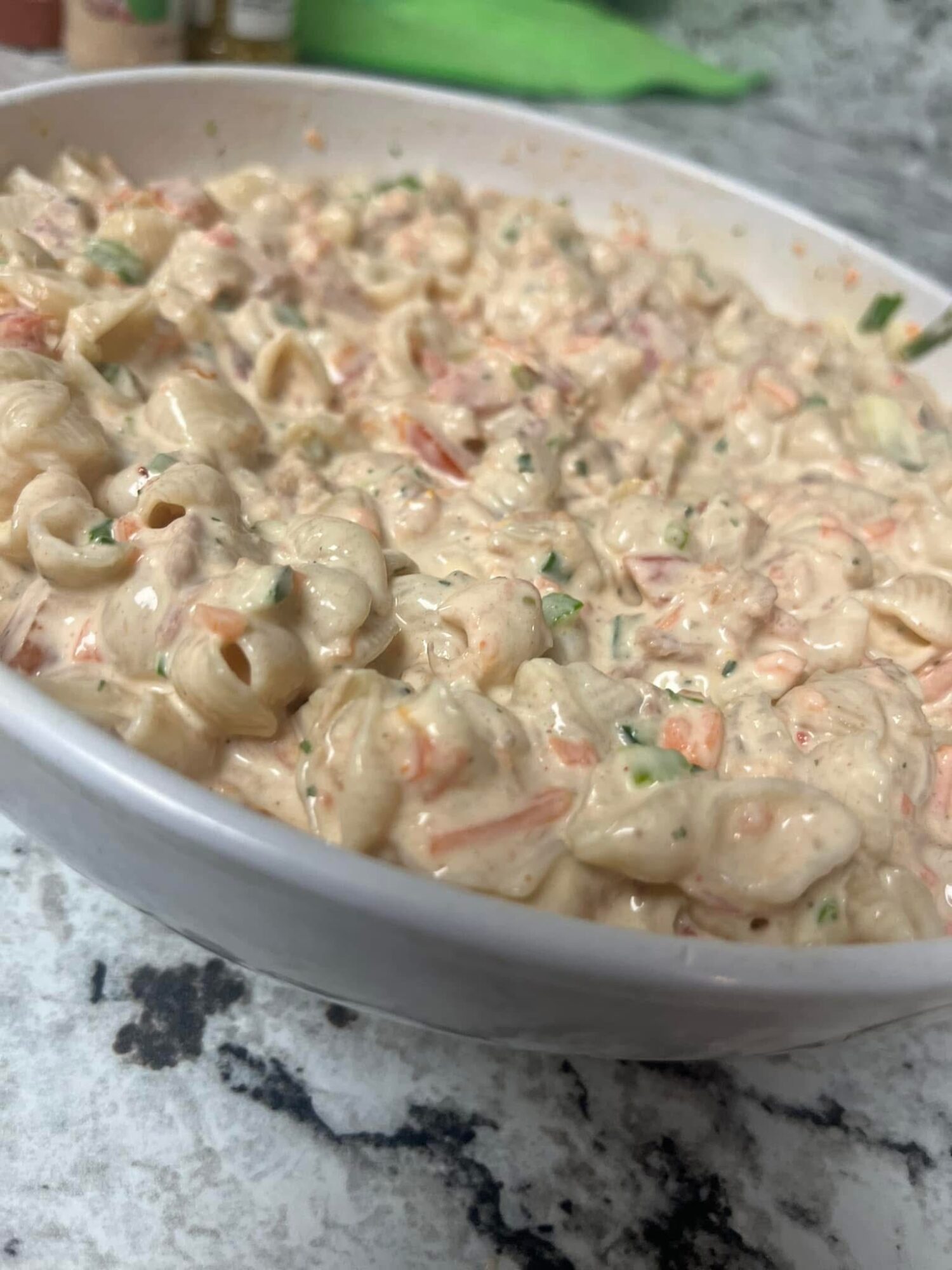 Creamy pasta salad with vegetables in a white bowl on a marble surface.