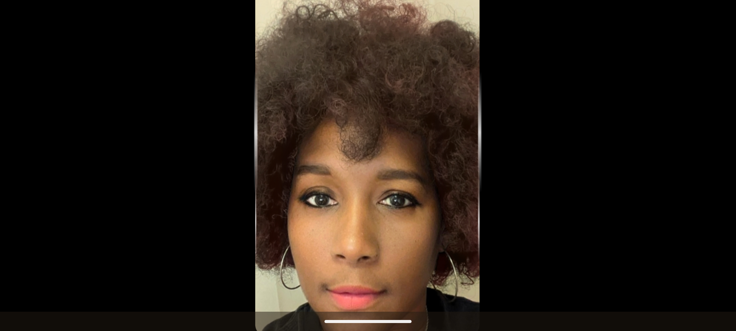 Close-up of a woman with curly hair and earrings, looking directly at the camera.