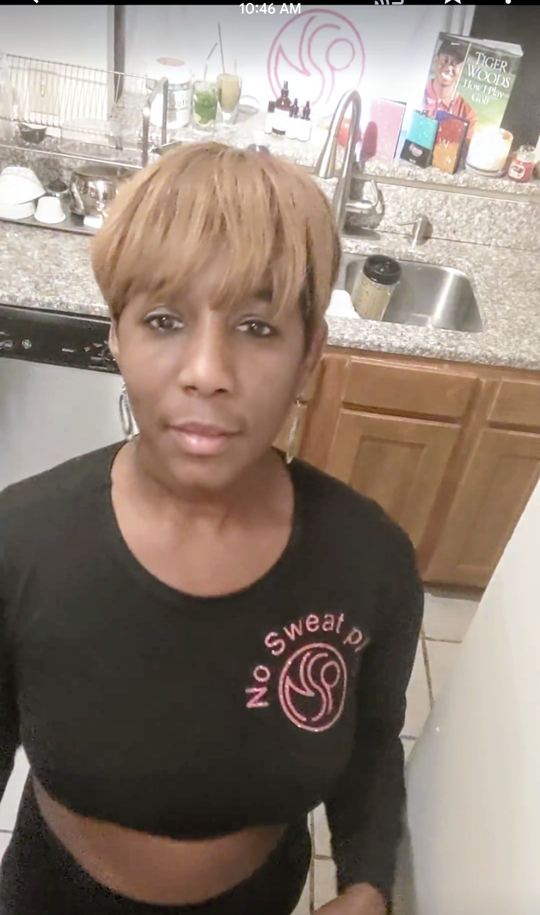 Woman with short blonde hair in a black shirt standing in a kitchen with a sink and cabinets behind her.