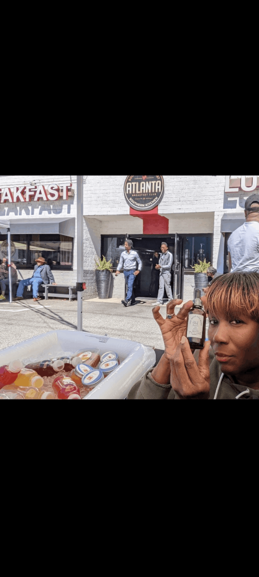 Child with brown hair and a striped shirt eating food outdoors, with a city street and people in the background.