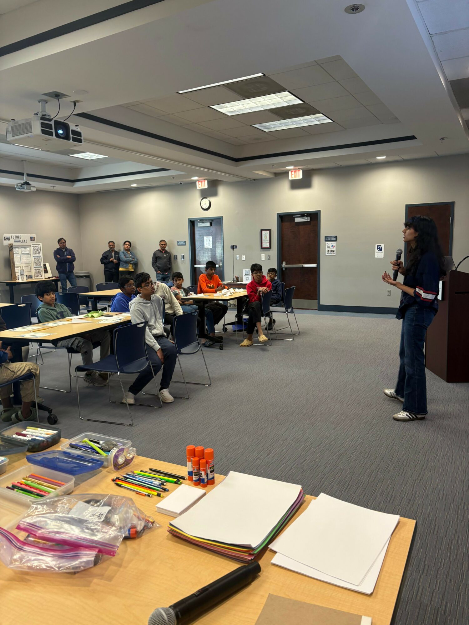 People gathered around a table in a conference room with notebooks and supplies, some standing and some seated.