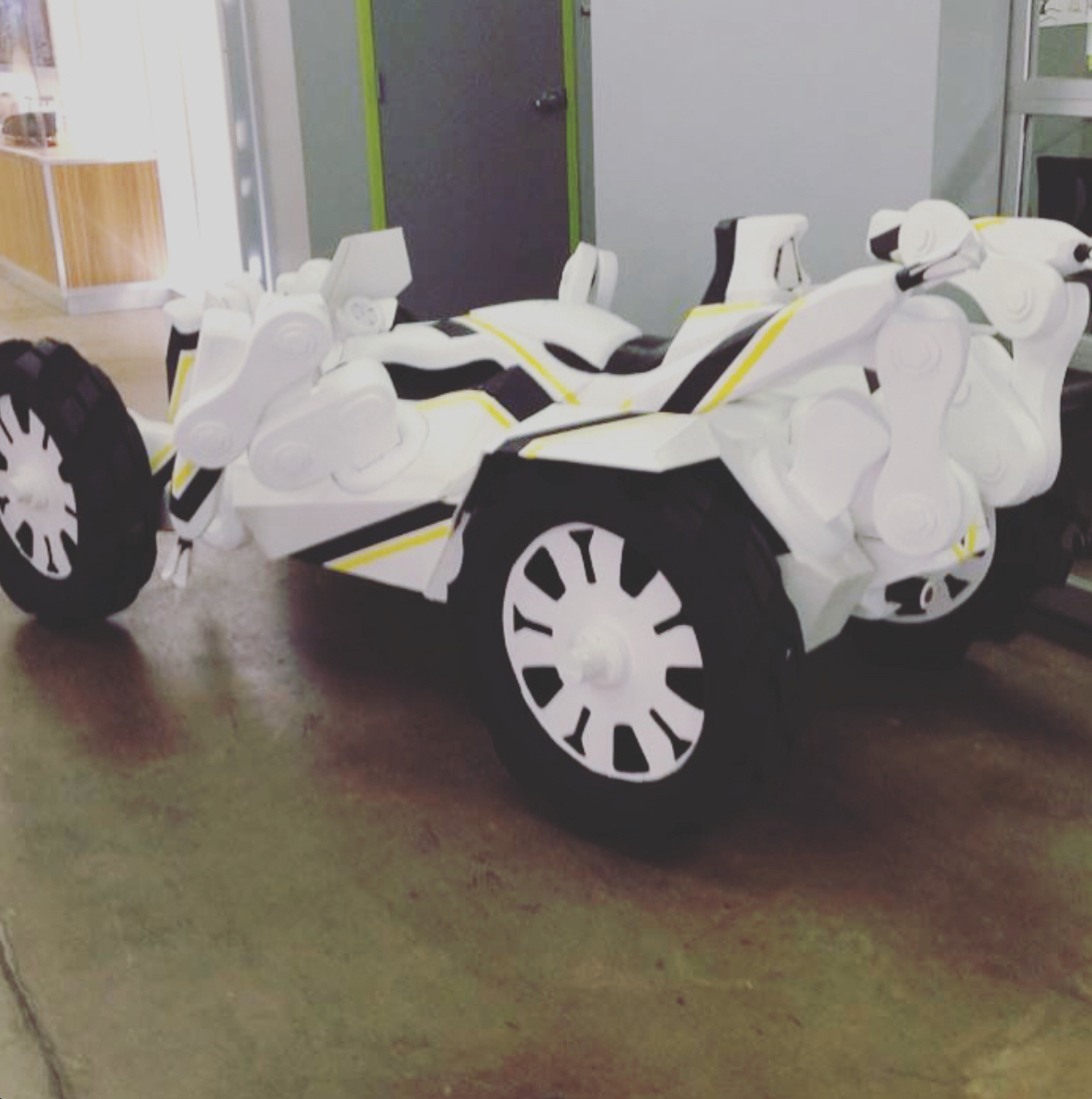 White and black toy race car with large wheels, placed indoors on a floor, with a door and window in the background.