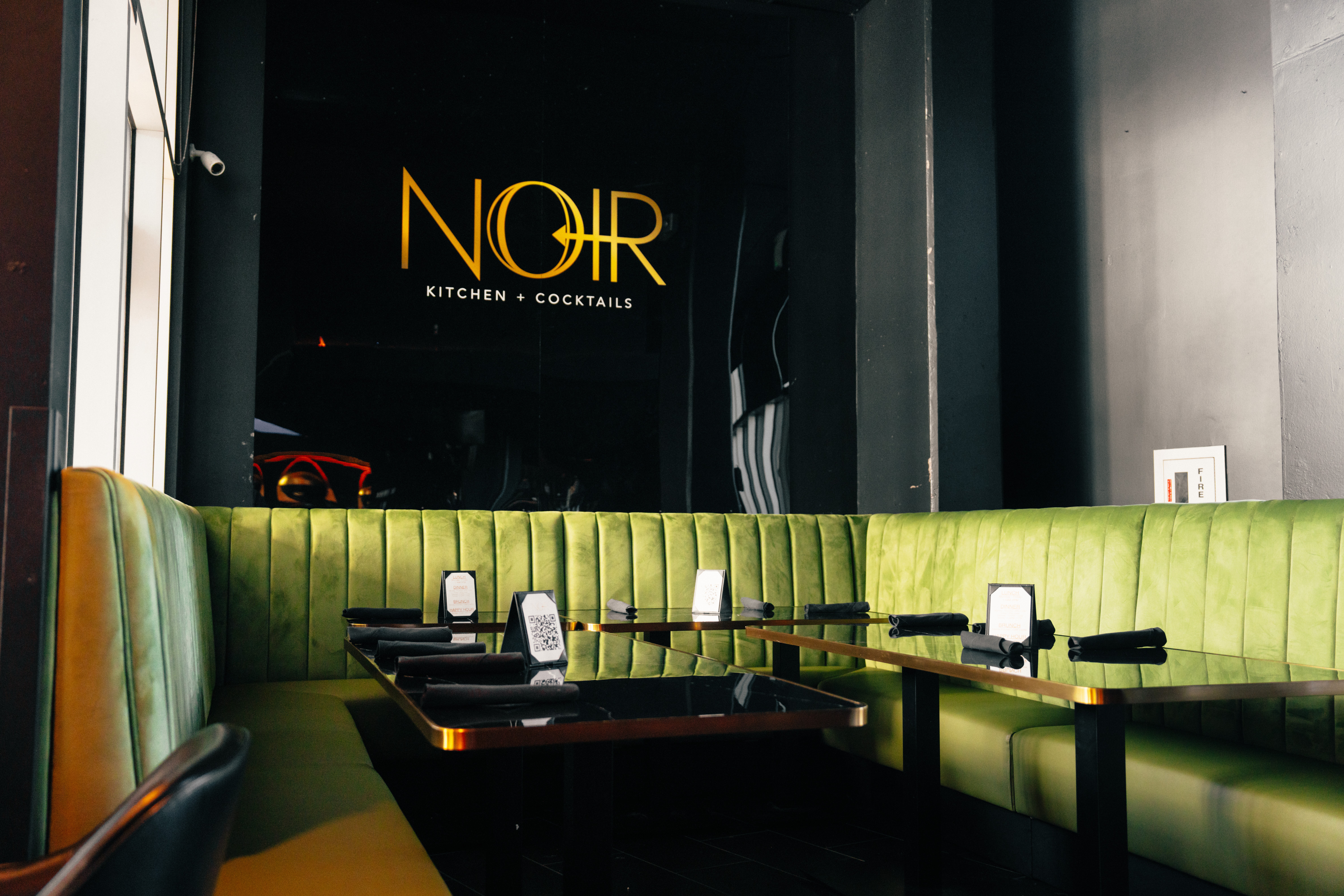 Interior of a restaurant with green seating and a dark wall with a neon sign reading 'NOIR'.