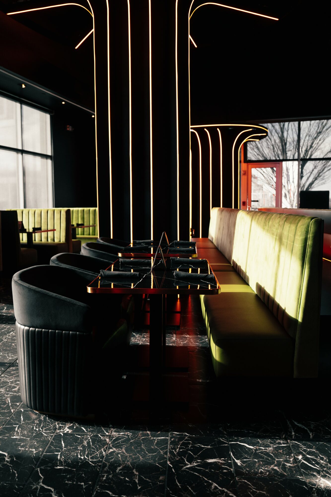 Interior of a modern lounge with illuminated vertical lines, black seating, and large windows showing trees outside.