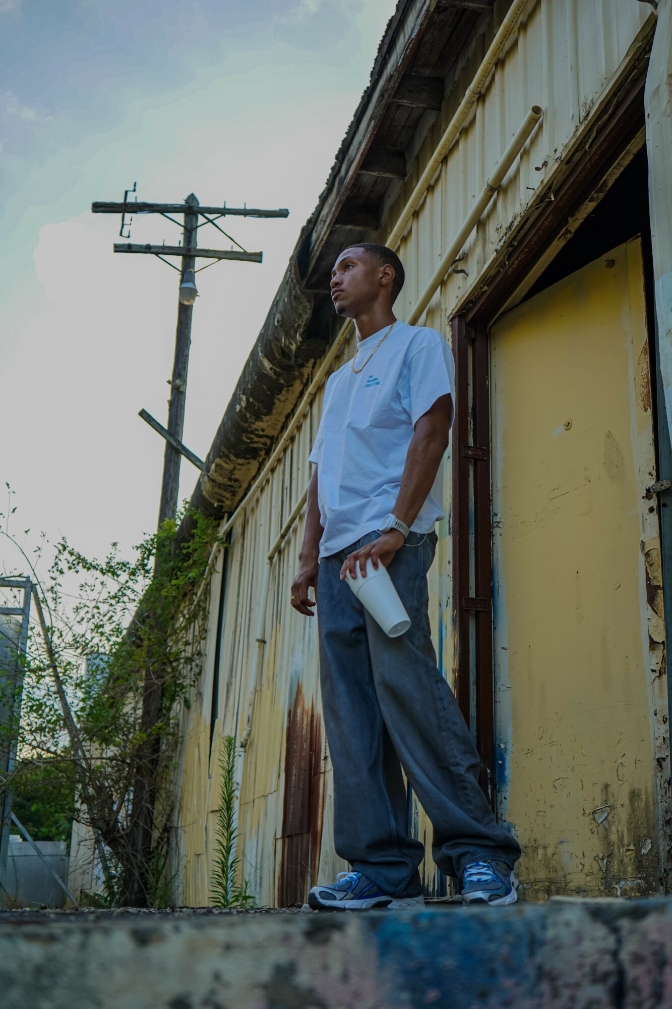 Young man standing outside a weathered building holding a water bottle, with a utility pole in the background.