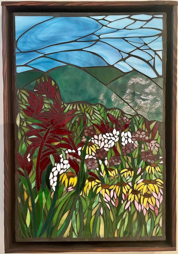 Colorful stained glass window depicting a landscape with blue sky, green hills, and various flowers in red, white, yellow, and pink.