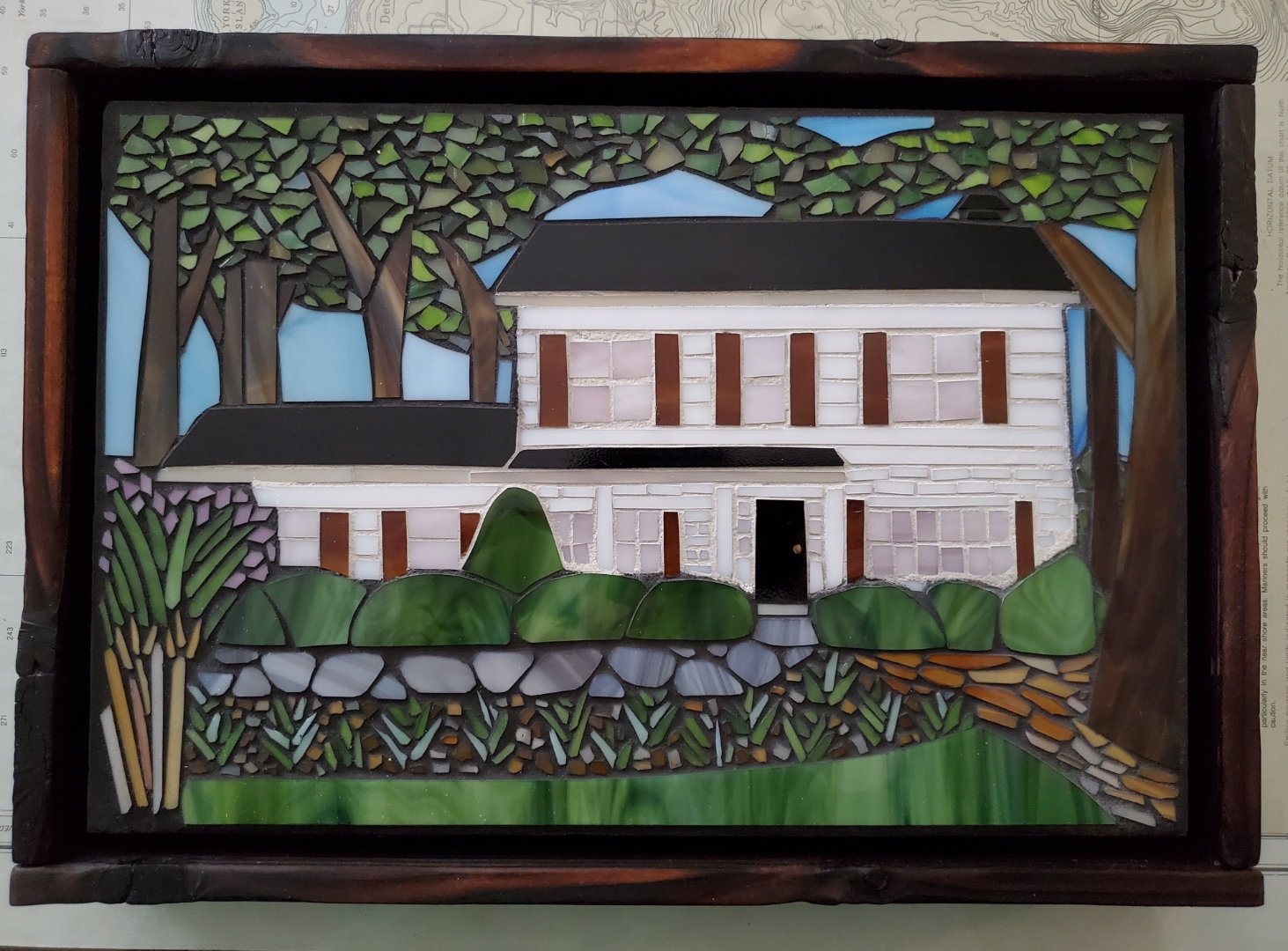 Colorful stained glass depiction of a house surrounded by trees and greenery, with a pathway leading to the entrance.