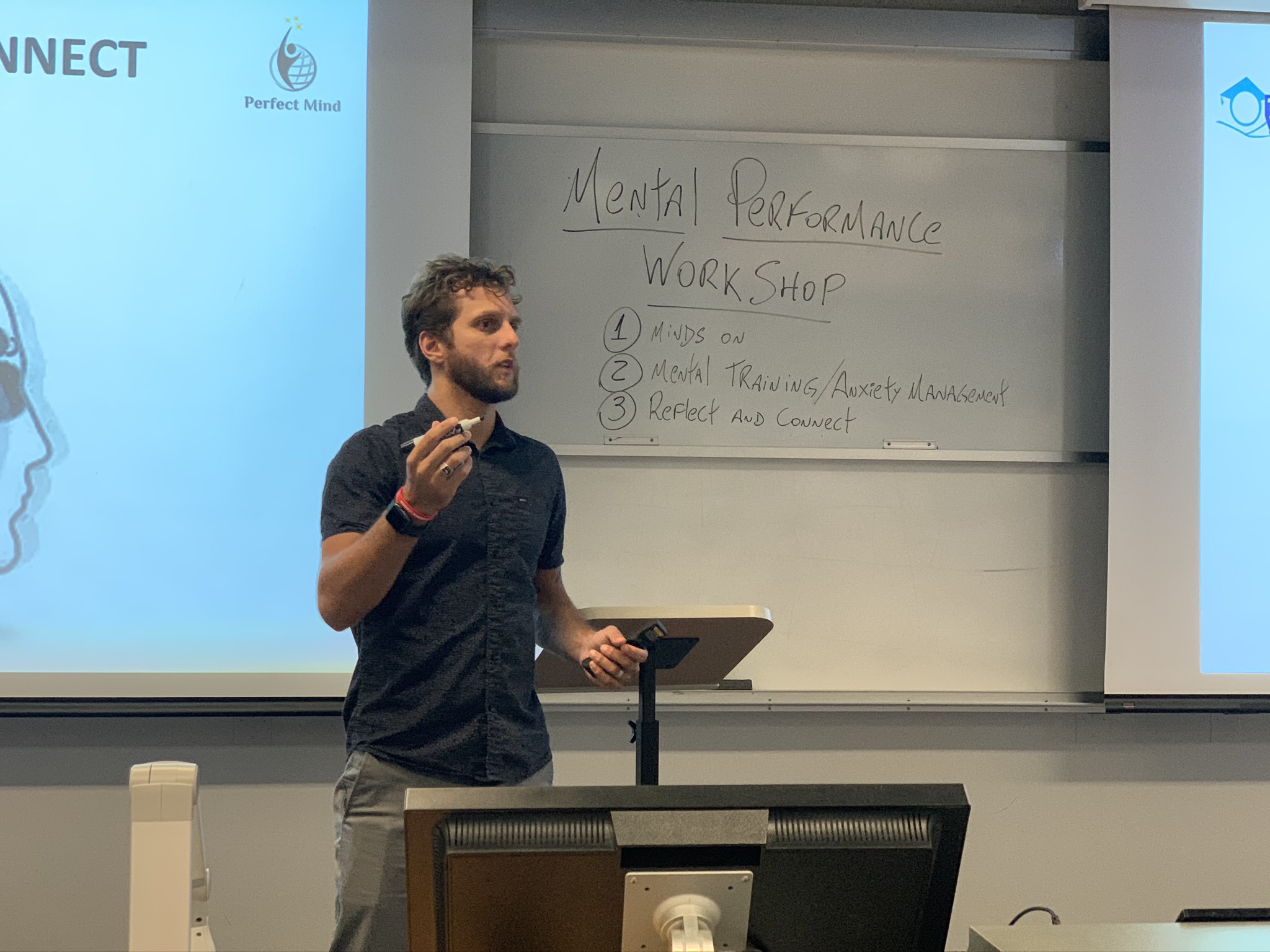 Man standing in front of whiteboard, holding marker, presenting during workshop, with text on whiteboard reading 'Mental Performance WORKSHOP'.