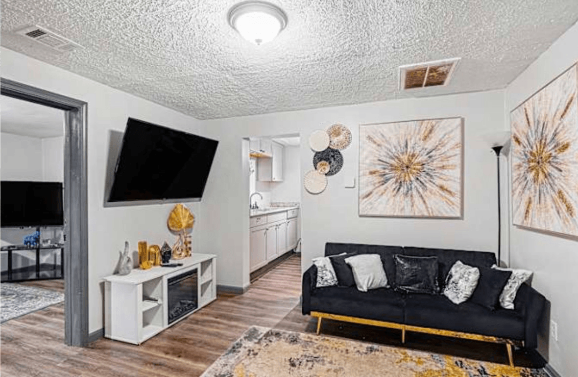 Living room with black sofa, wall art, TV, and doorway to another room, with hardwood floors and white walls.