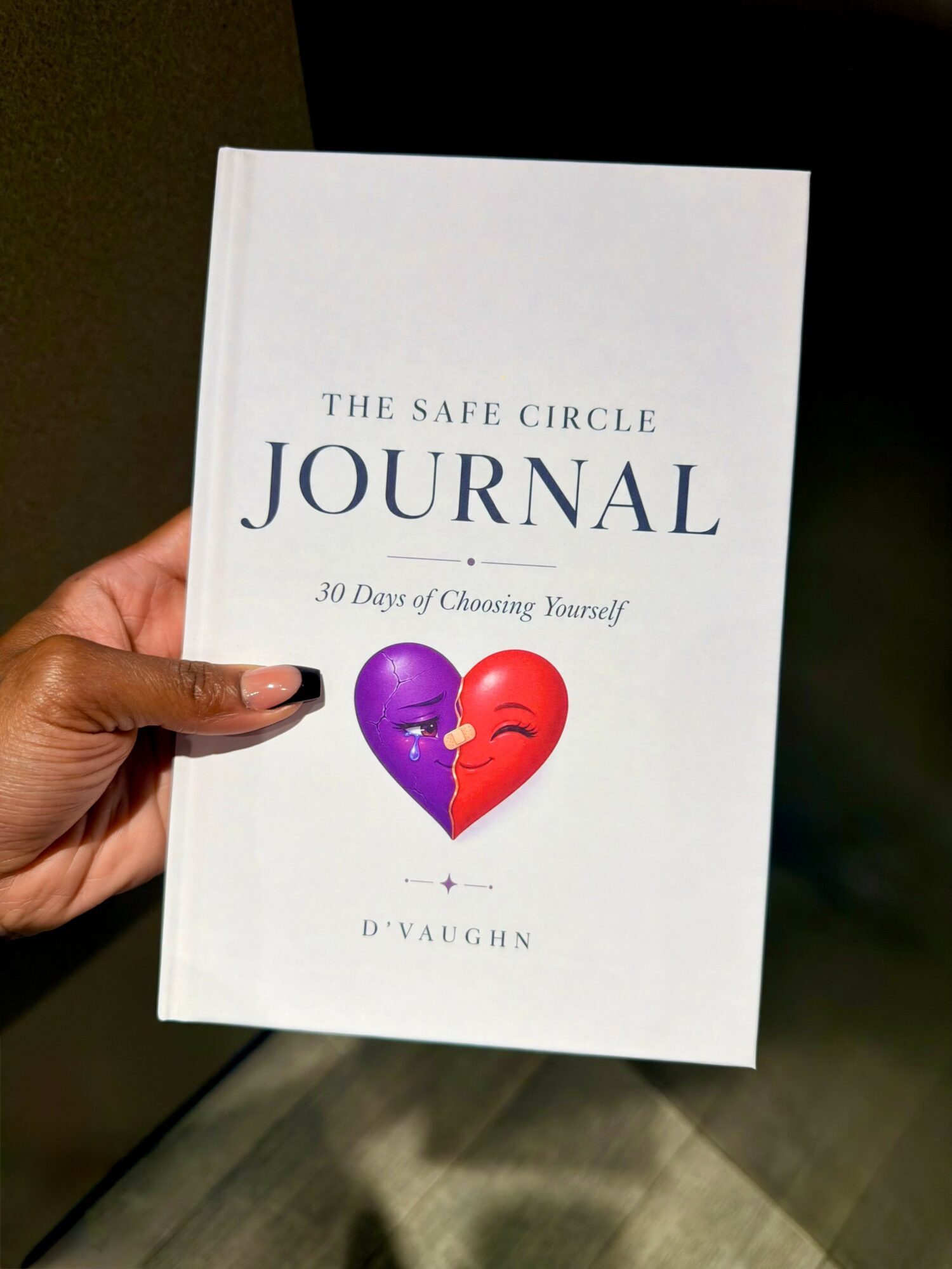 Hand holding a white journal titled 'The Safe Circle Journal' with a purple and red heart illustration.